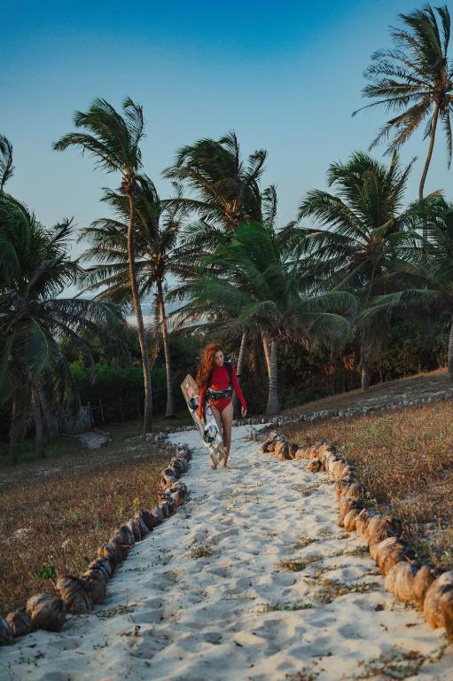 A sandy path through the palms with a kitesurfer walking toward the sea